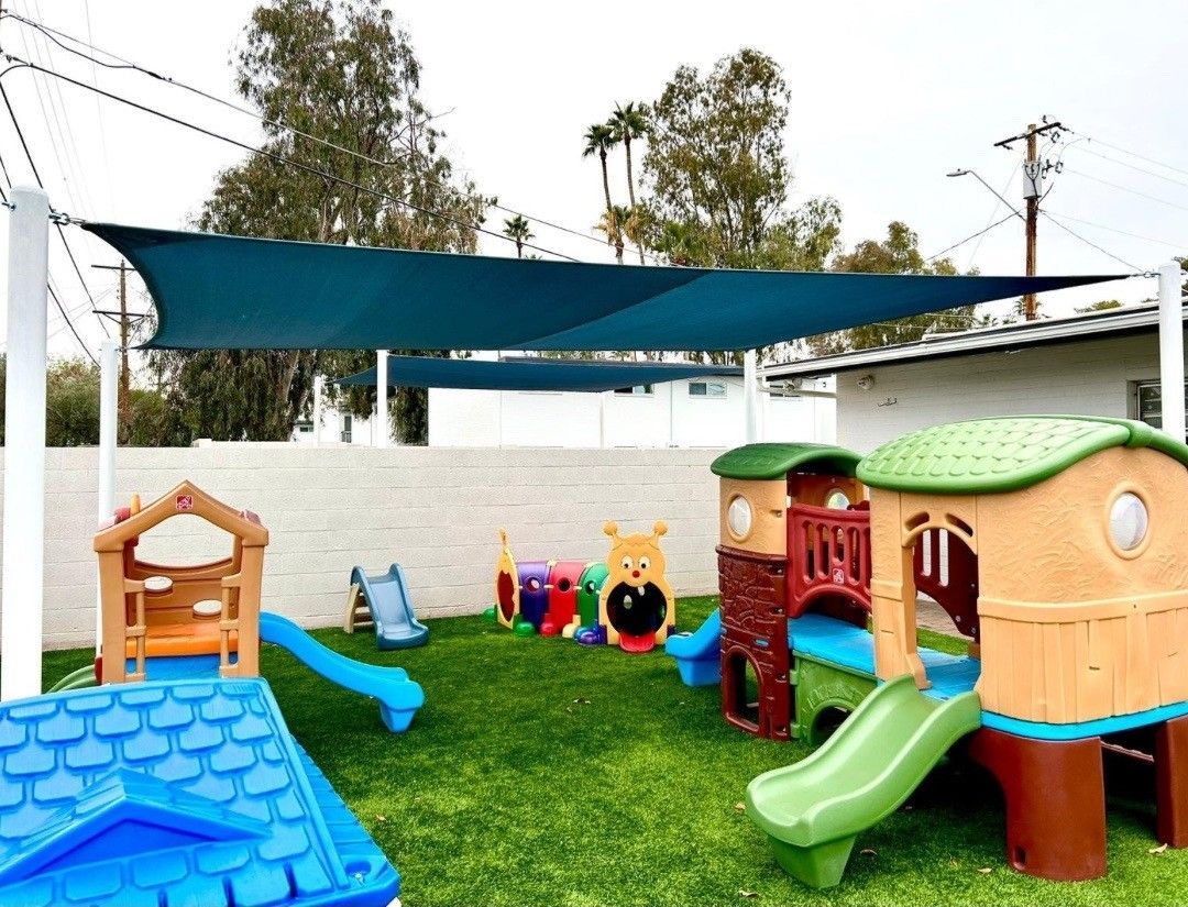 A playground with a slide and a house under a blue umbrella.