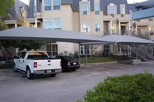 A white truck is parked under a carport in front of a large house.