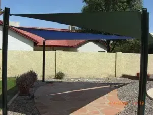 A blue shade sail is sitting on a patio in front of a house.