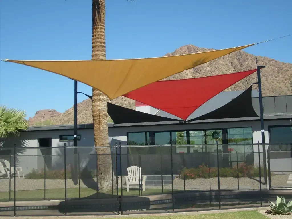 Three shade sails are hanging from a pole in front of a building