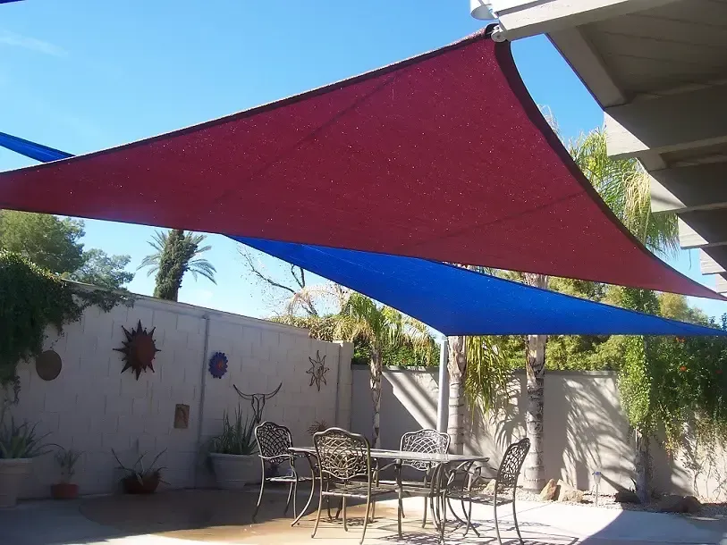 A red and blue shade sail is covering a table and chairs