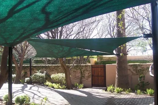 A green shade covering a parking lot with trees in the background