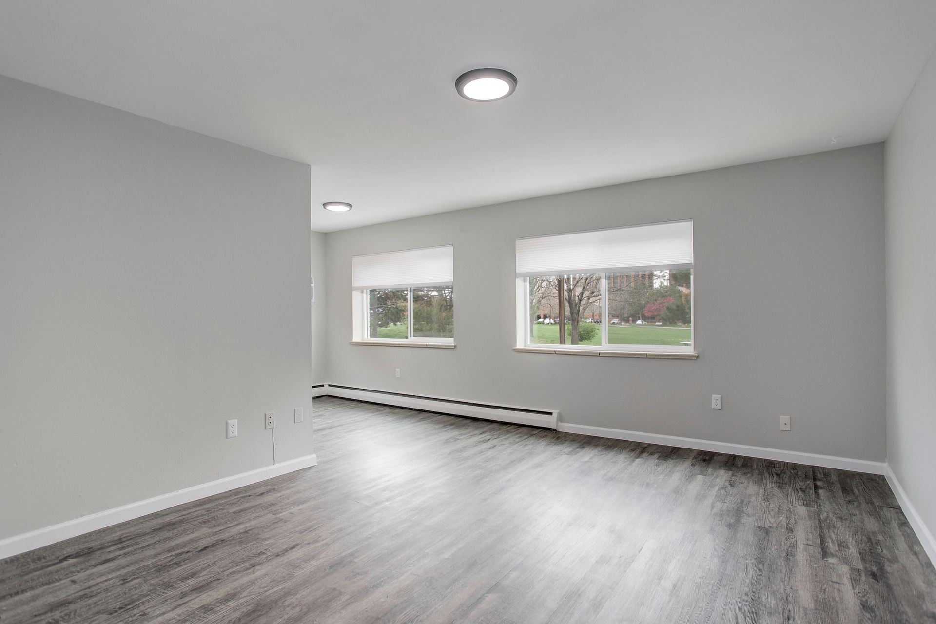 an empty living room with hardwood floors and two windows .