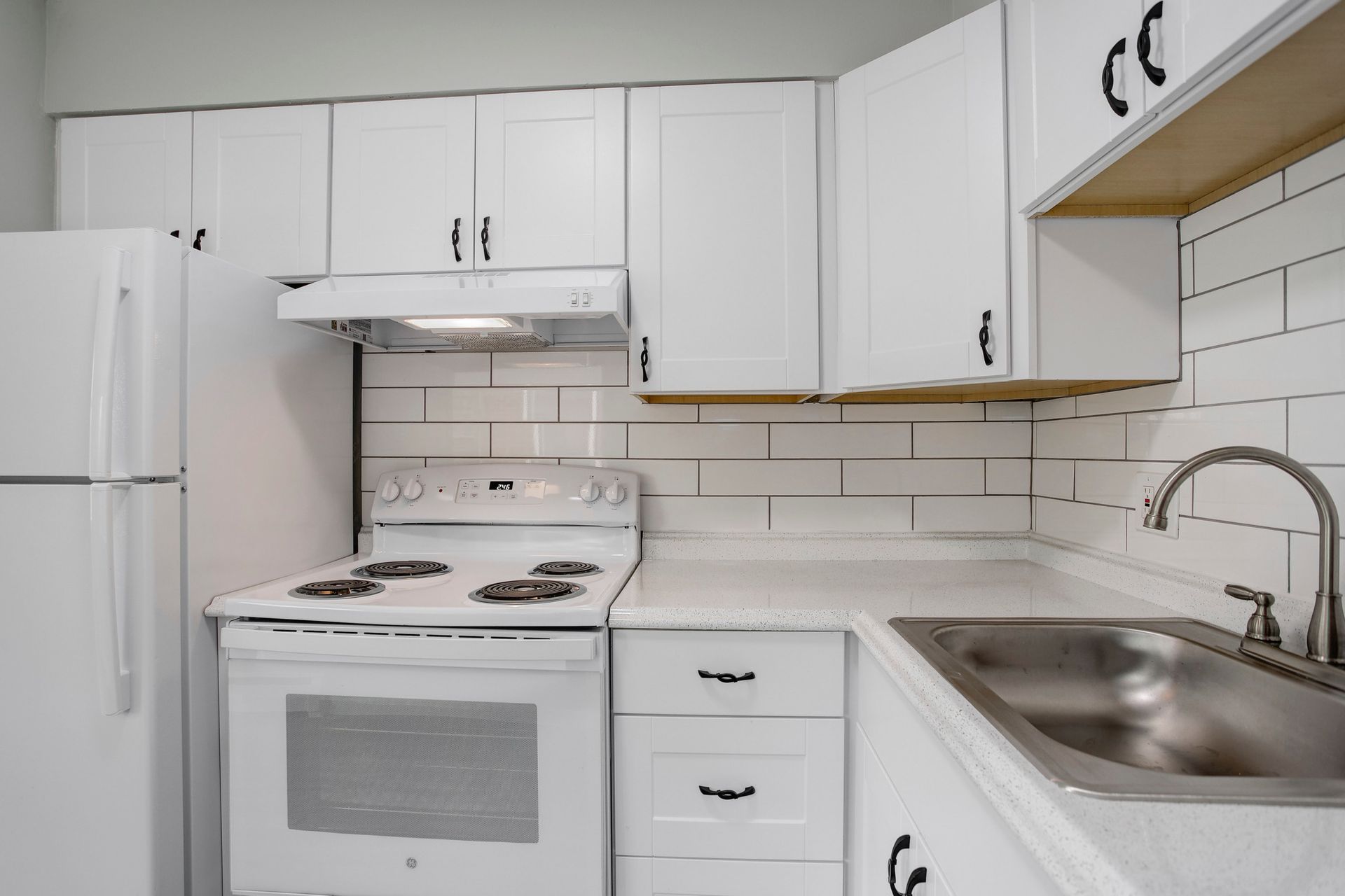 a kitchen with white cabinets , a stove , a refrigerator and a sink