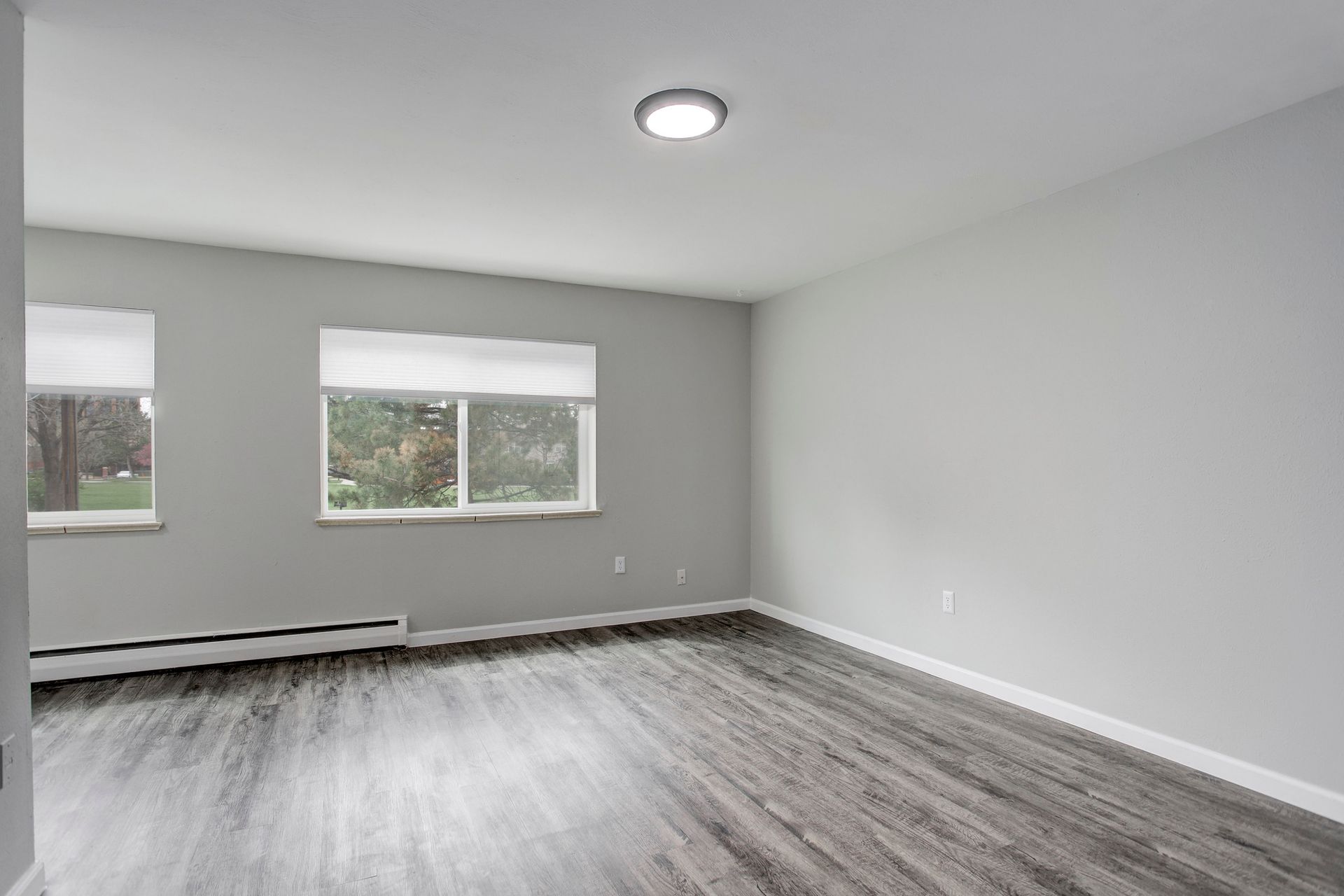 an empty living room with hardwood floors and two windows .