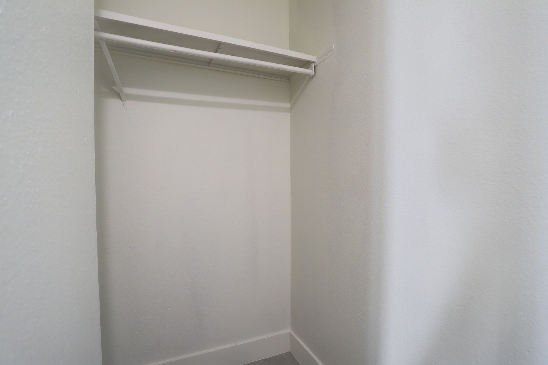 a closet with a shelf and clothes hanging on the wall .