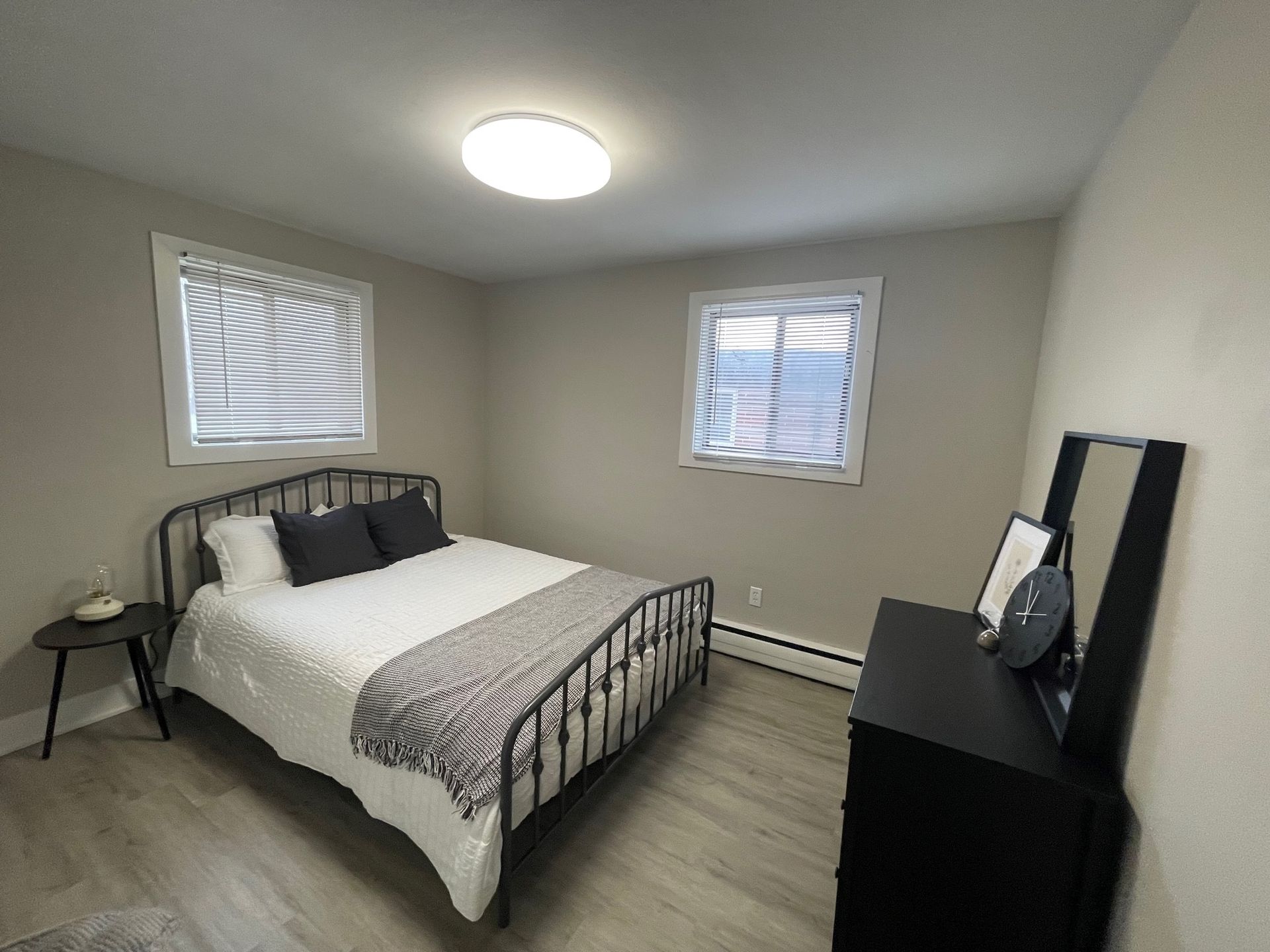 a bedroom with a bed , dresser , mirror and two windows .