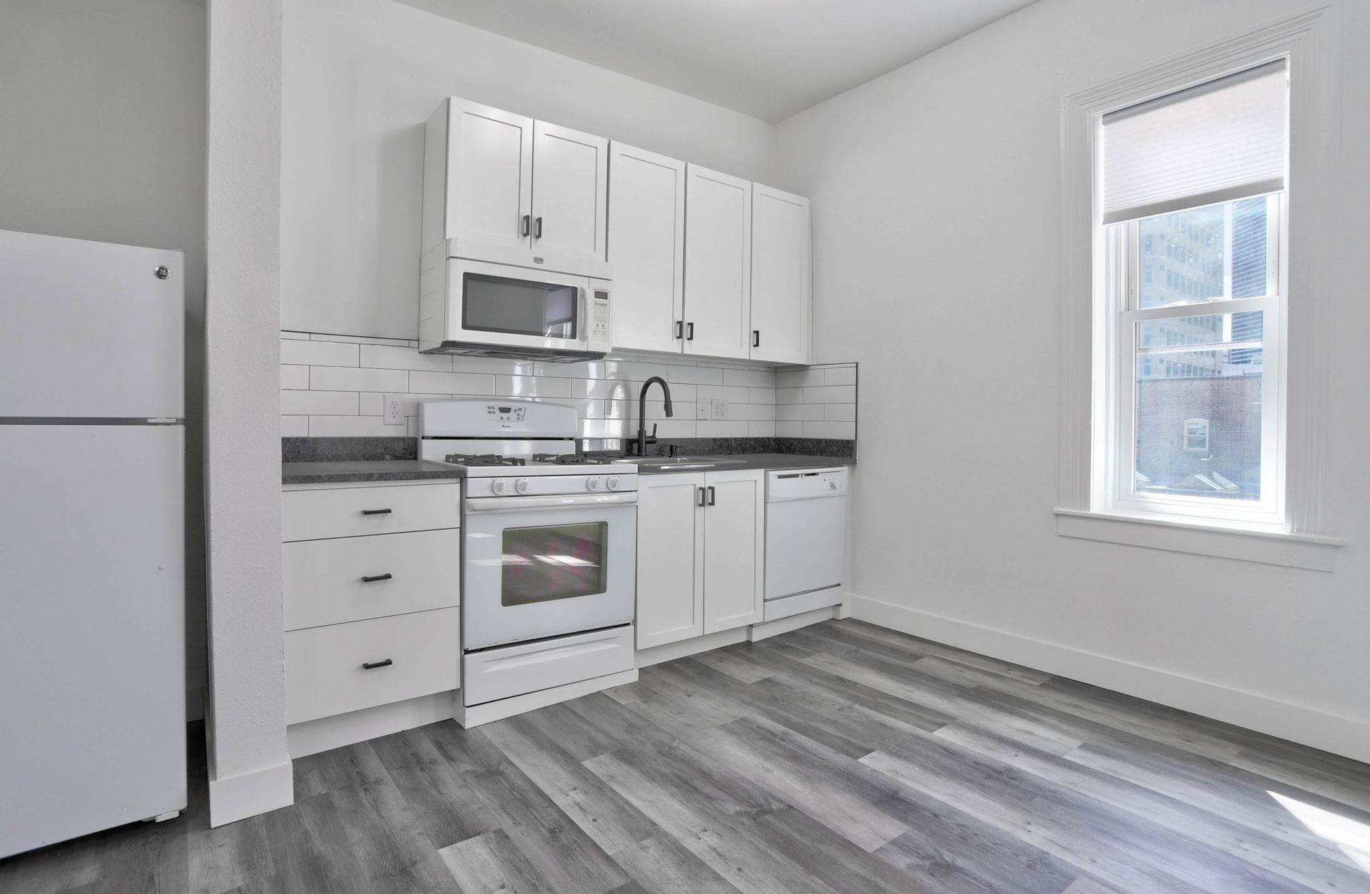 a kitchen with white cabinets , appliances , a refrigerator and a window .