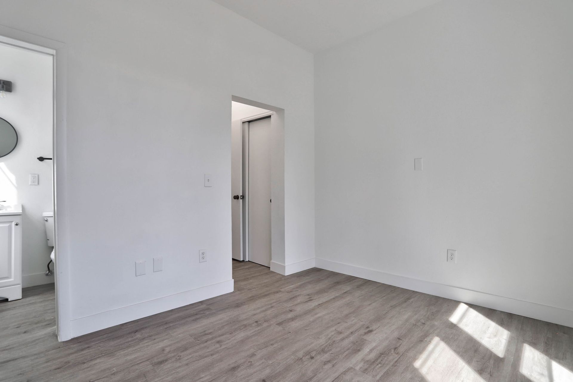 an empty bedroom with hardwood floors and white walls .