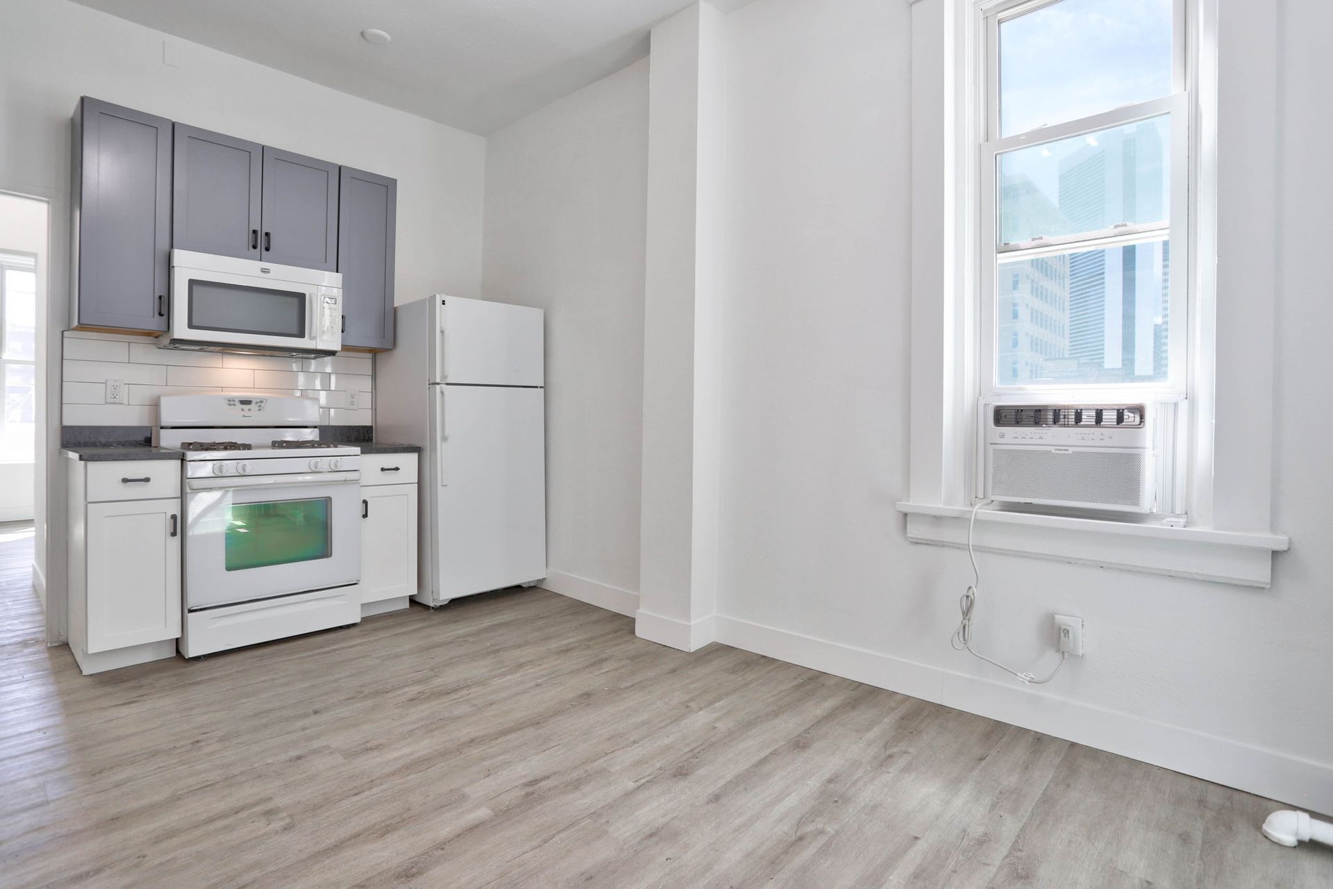 an empty kitchen with a refrigerator , stove , microwave and window .