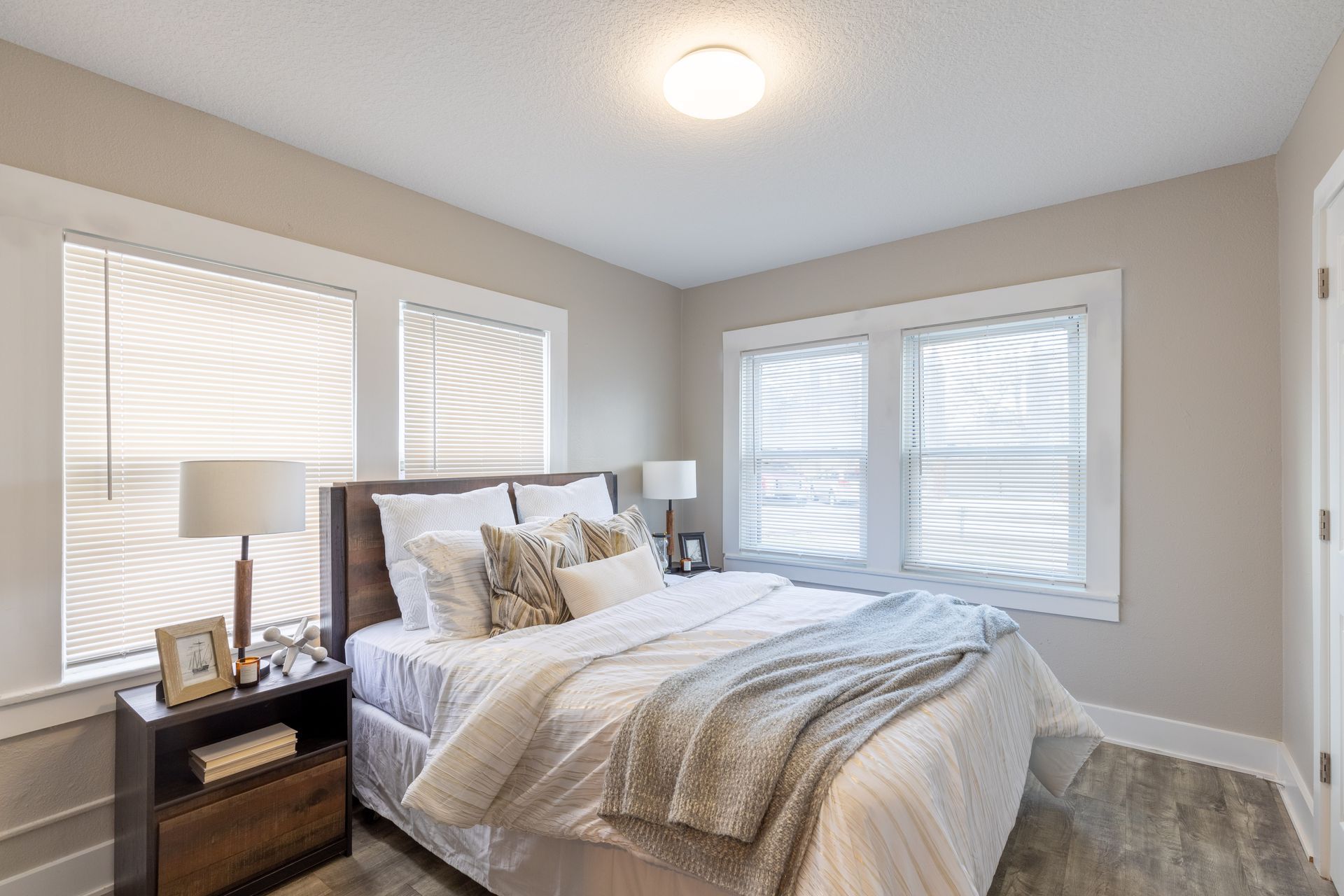 a bedroom with a bed , nightstand , lamps and two windows .