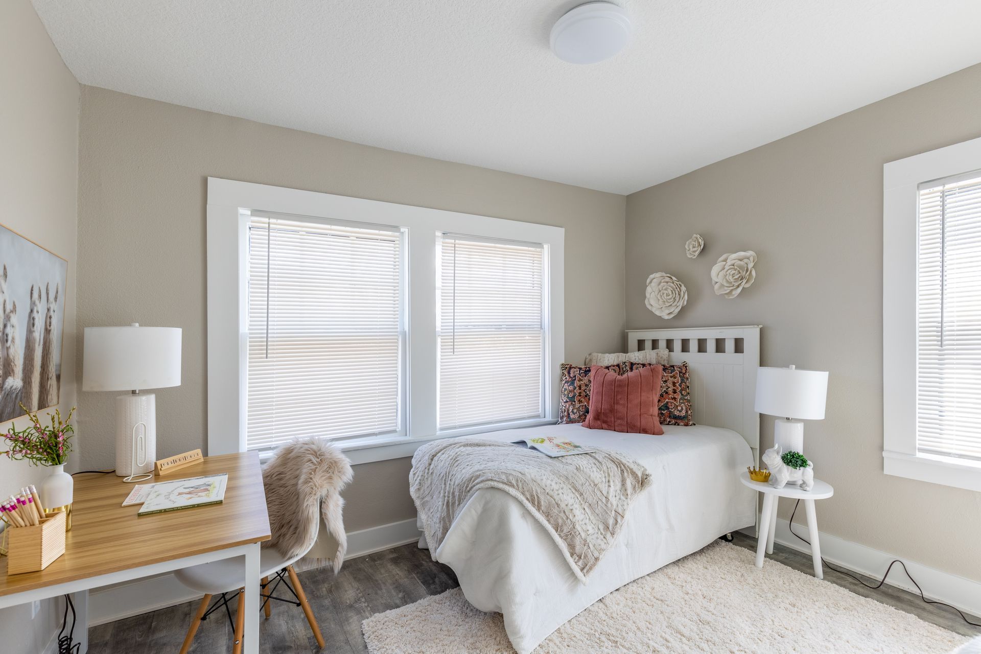 a bedroom with a bed , desk , chair and two windows .