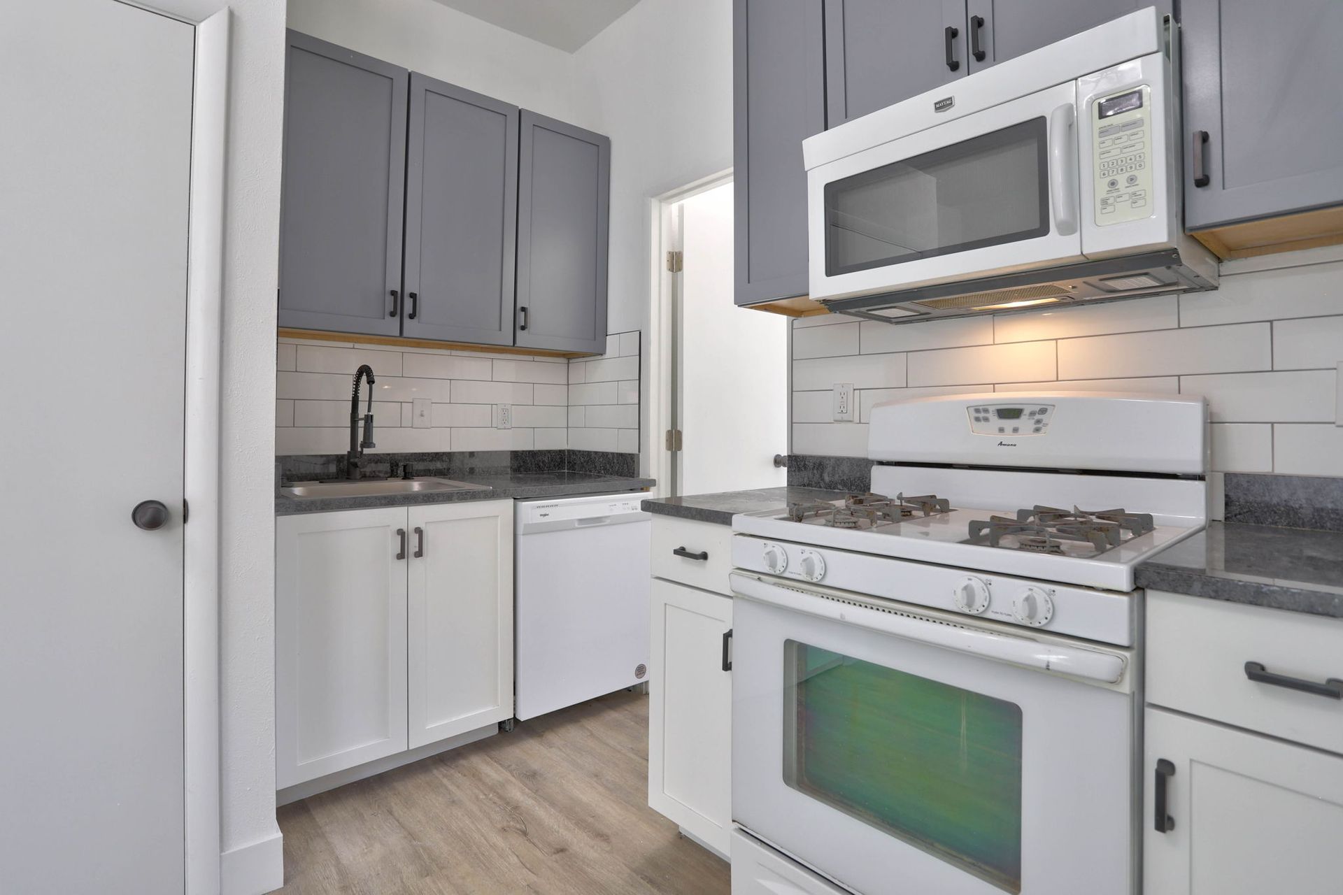 a kitchen with a stove , microwave , sink and cabinets .
