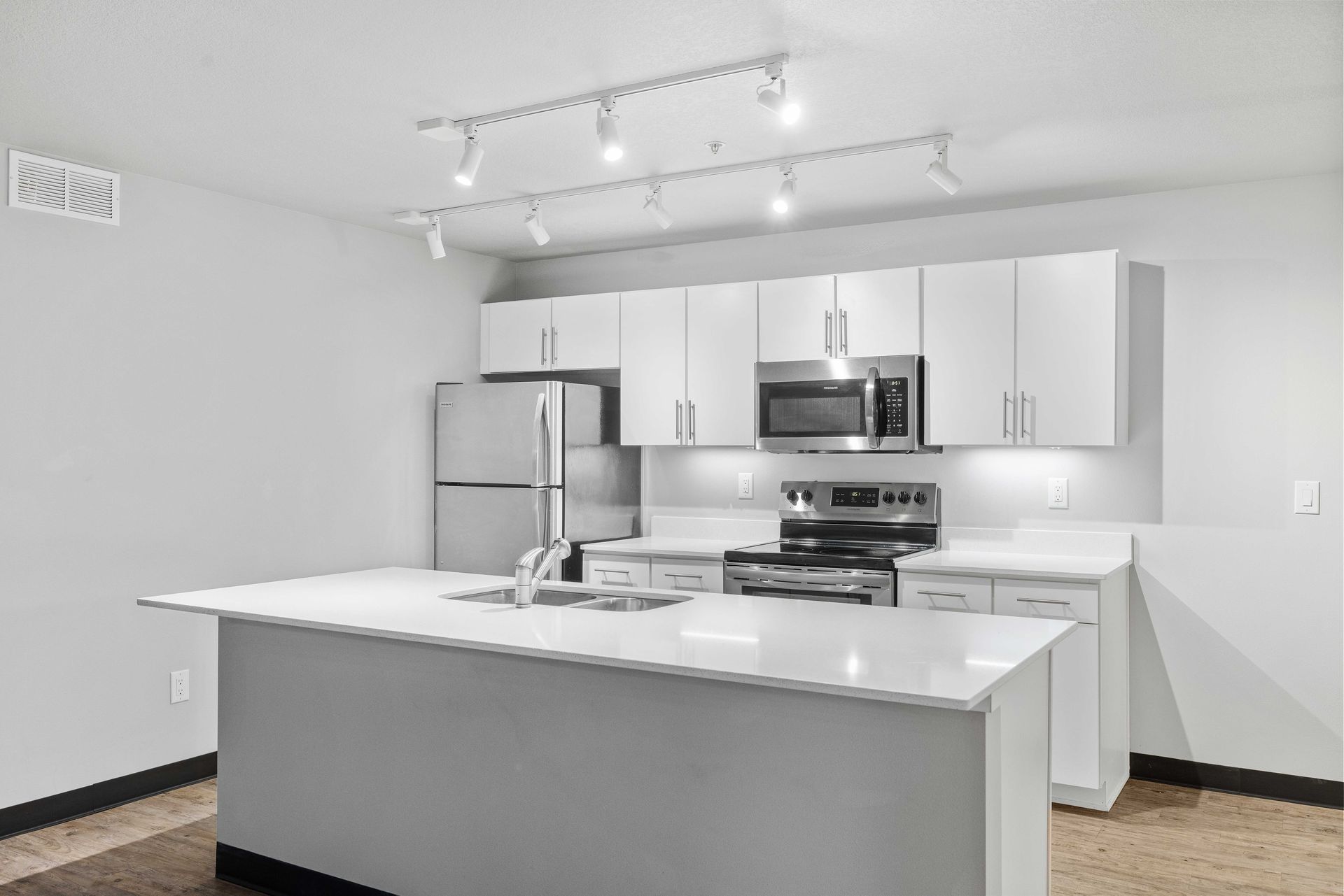 an empty living room with hardwood floors and a kitchen in the background .