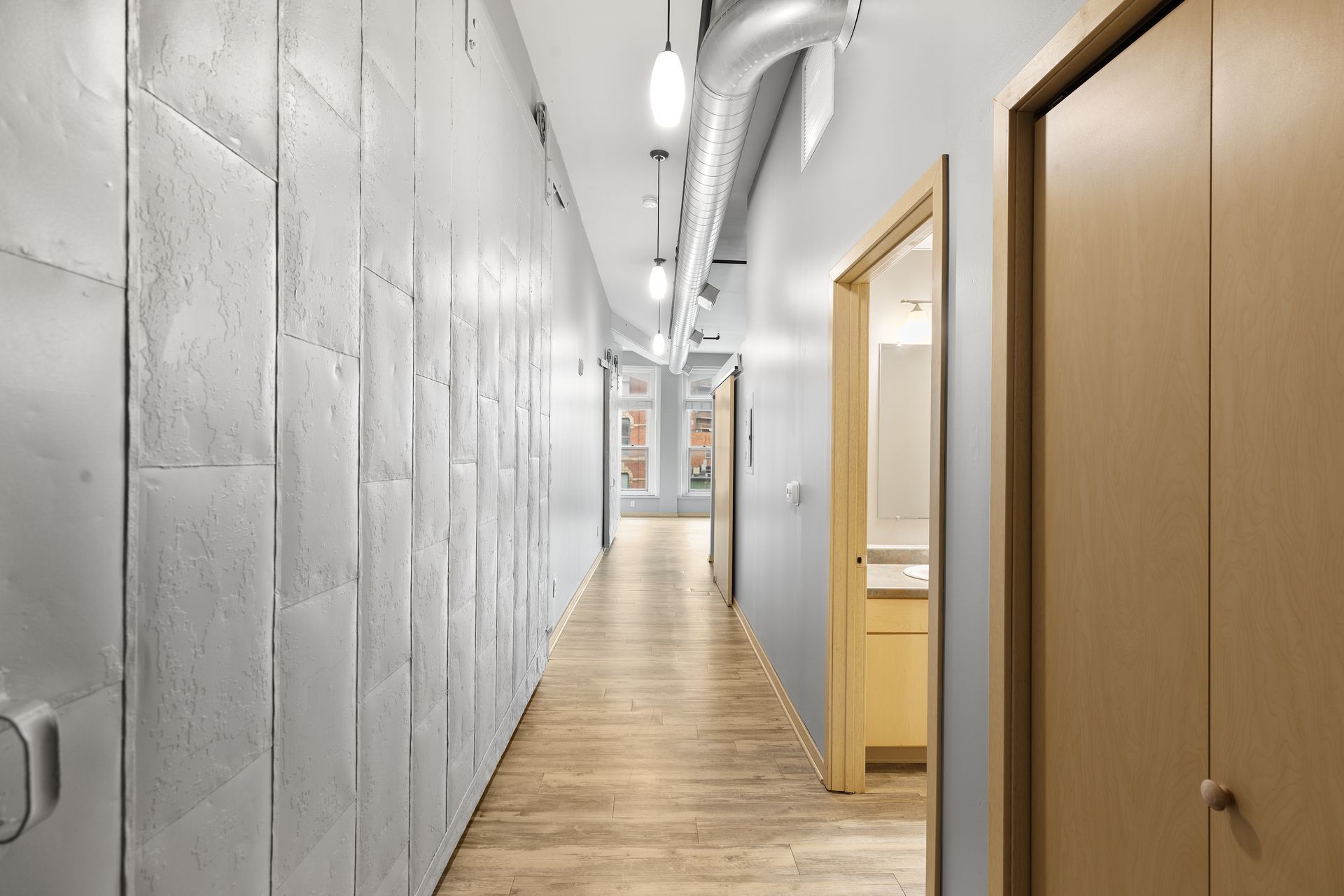 a long hallway with white walls and wooden floors leading to a bathroom .