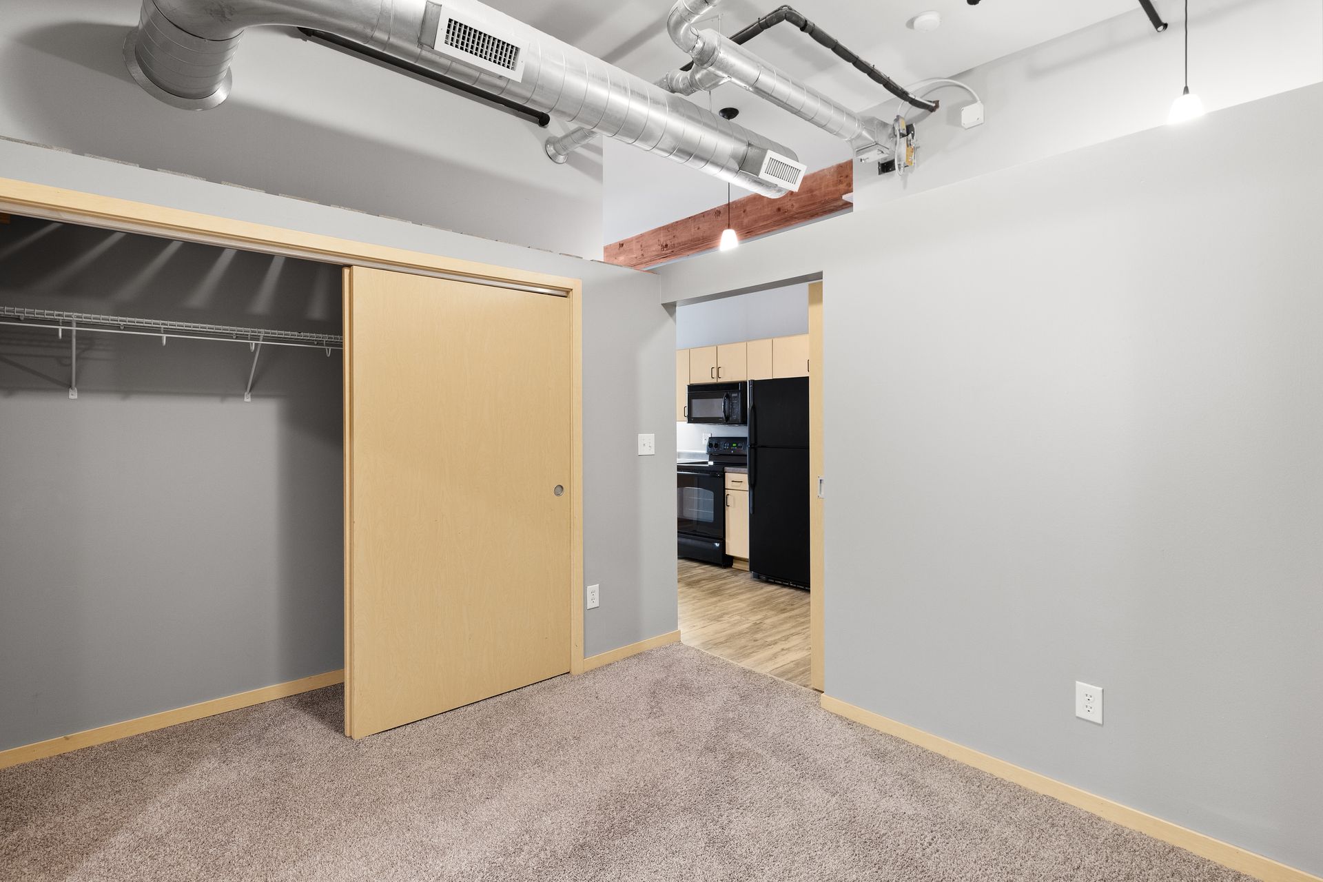 an empty room with a closet and a kitchen in the background .