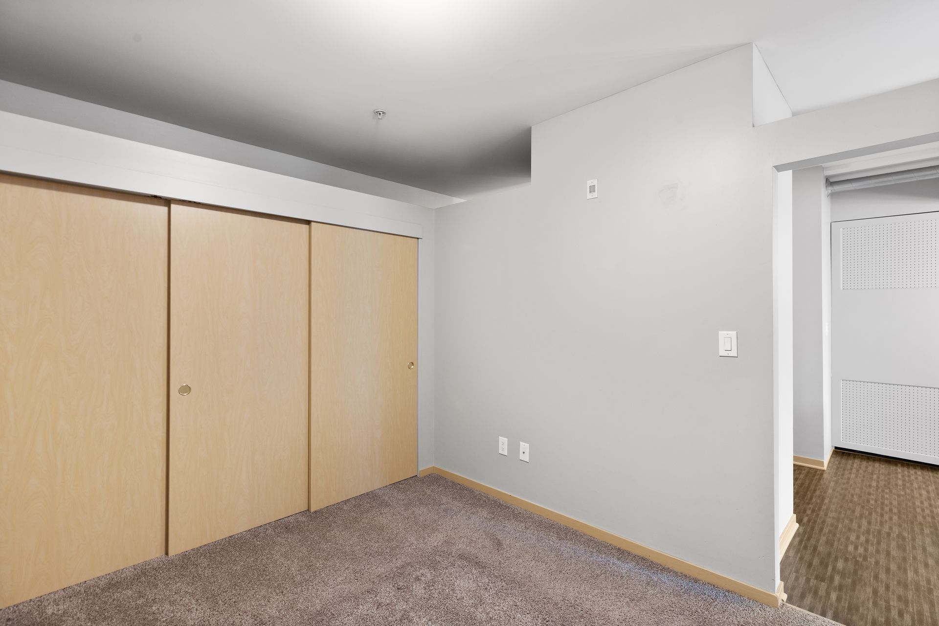 an empty room with a carpeted floor , wooden doors , and a closet .