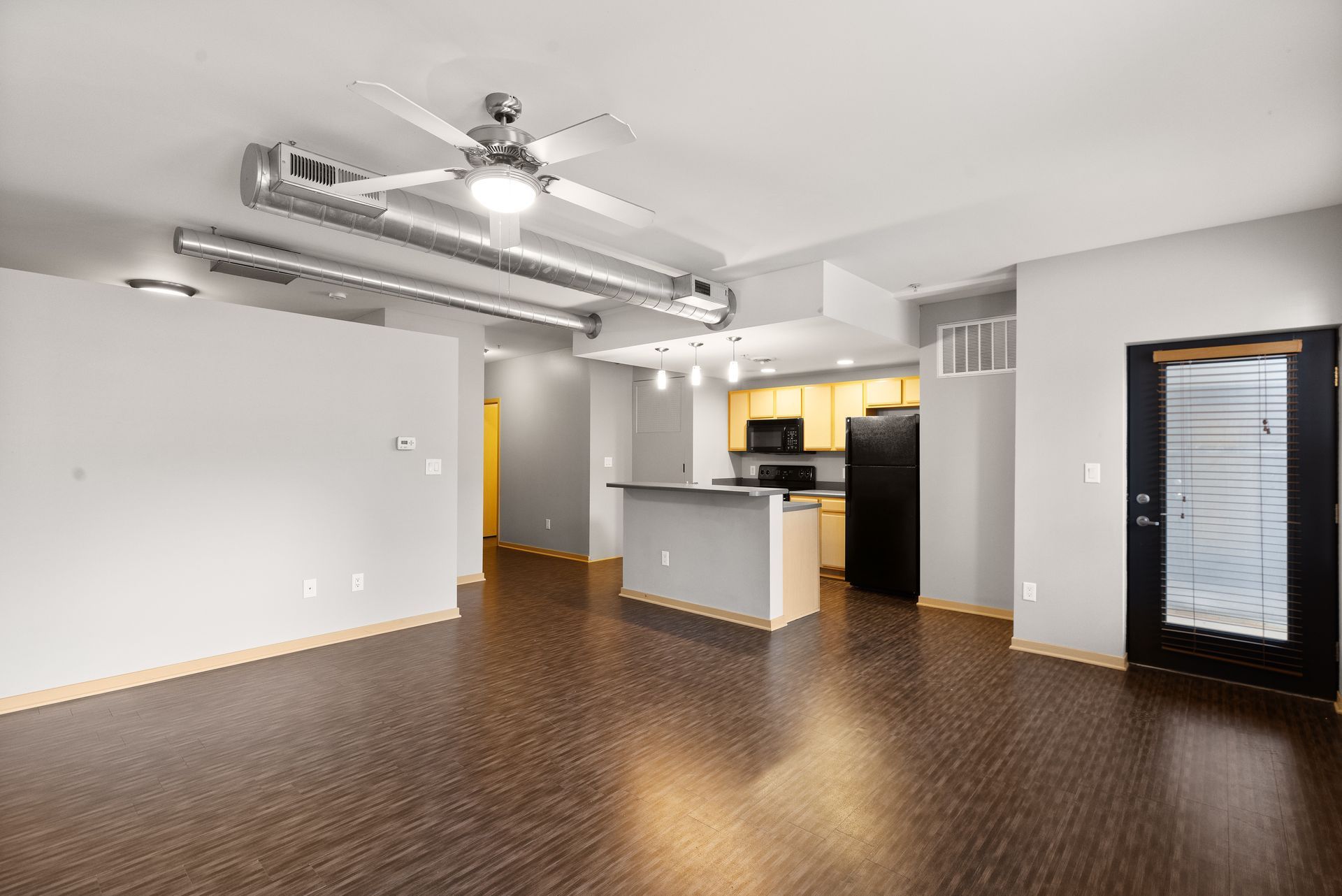 there is a ceiling fan in the living room and a kitchen in the background .