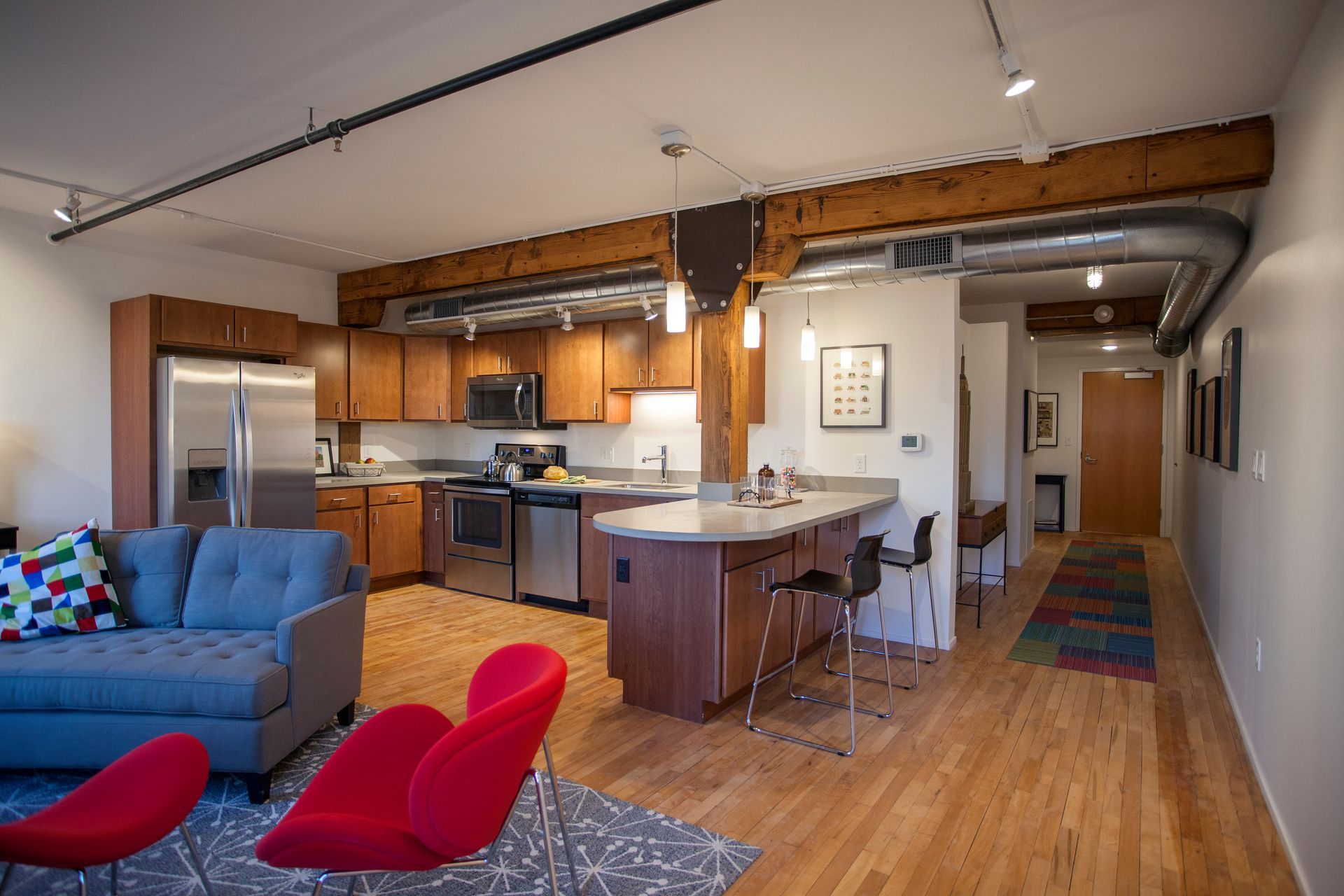a living room with a couch and red chairs and a kitchen with stainless steel appliances