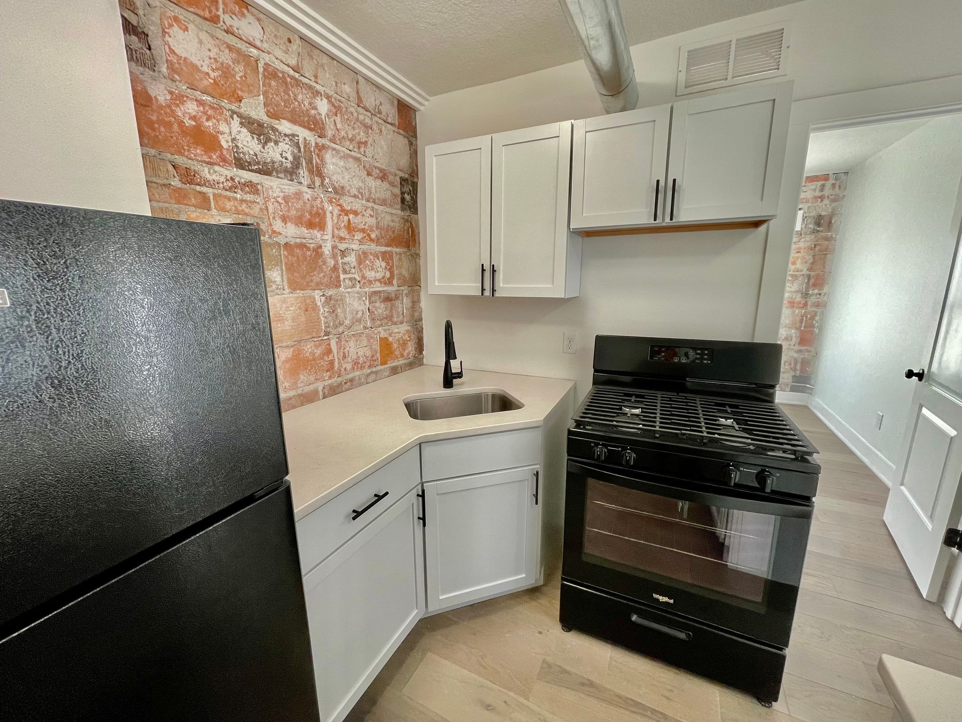 a kitchen with a stove , refrigerator , sink and brick wall .