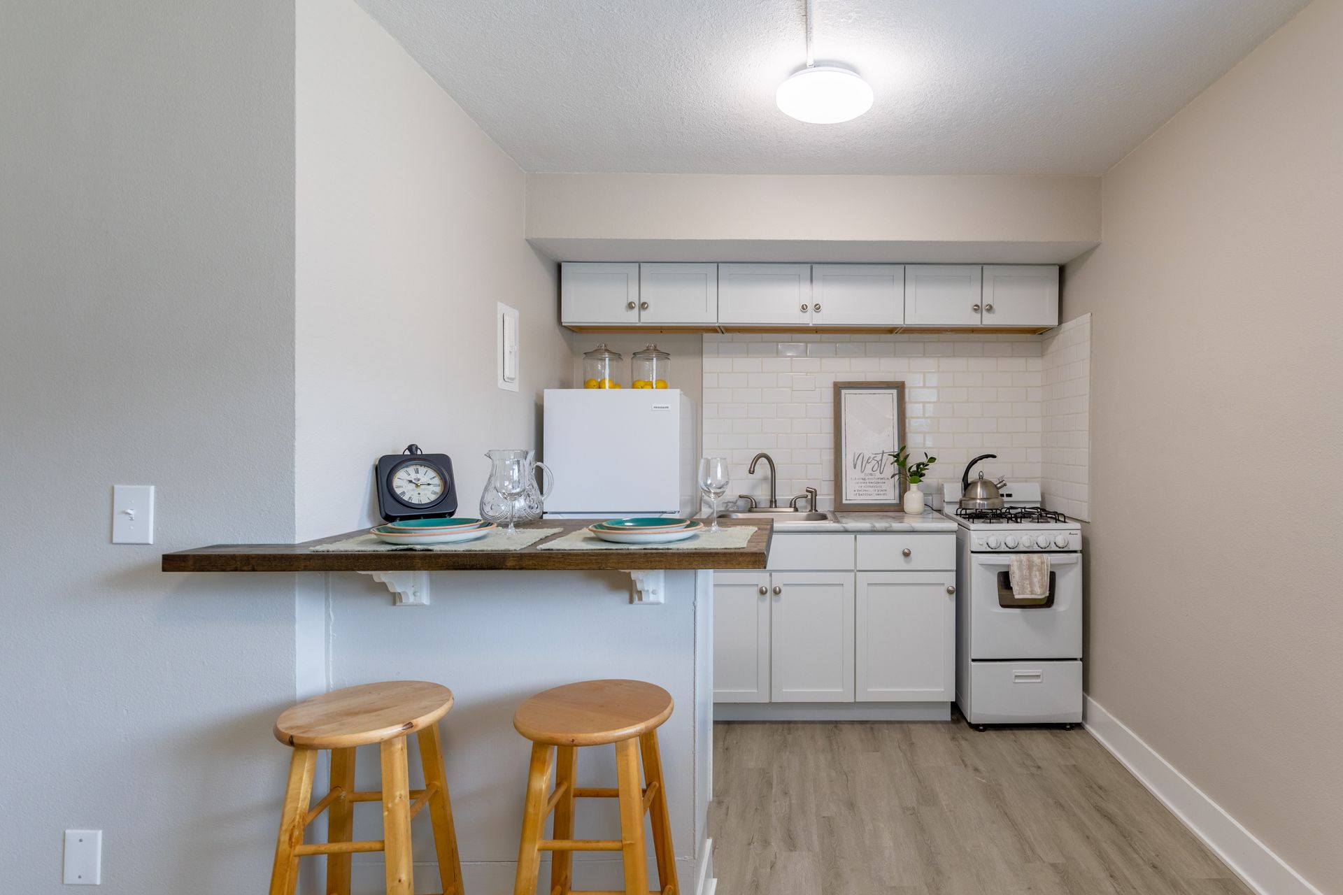 a kitchen with white cabinets , a stove , a sink , and two stools .