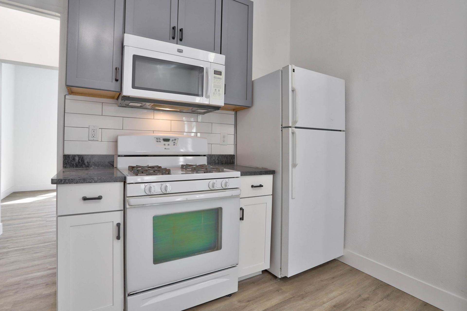 a kitchen with a stove , microwave , refrigerator and cabinets .