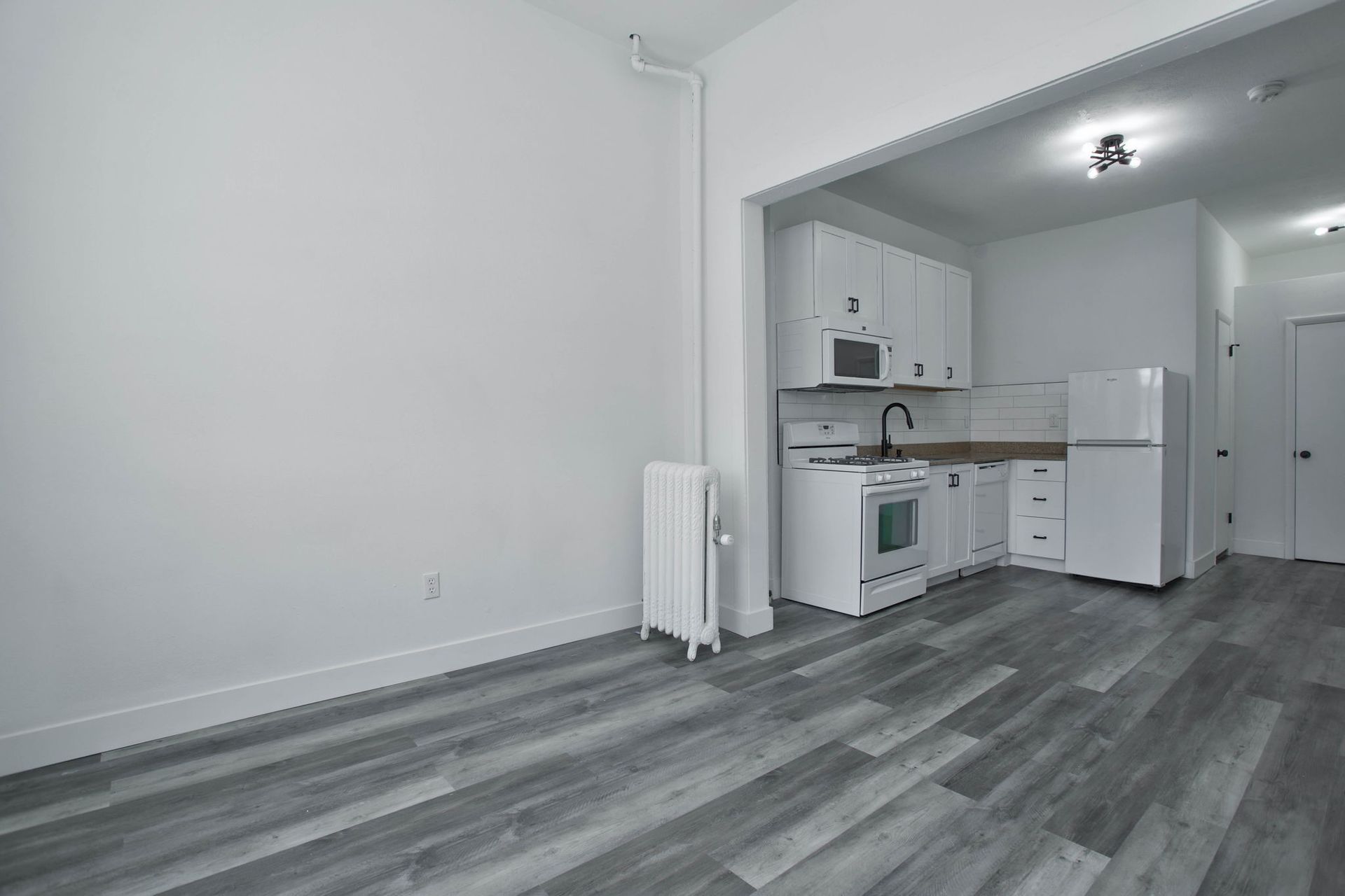 a kitchen with a refrigerator , stove , microwave and sink in an empty apartment .