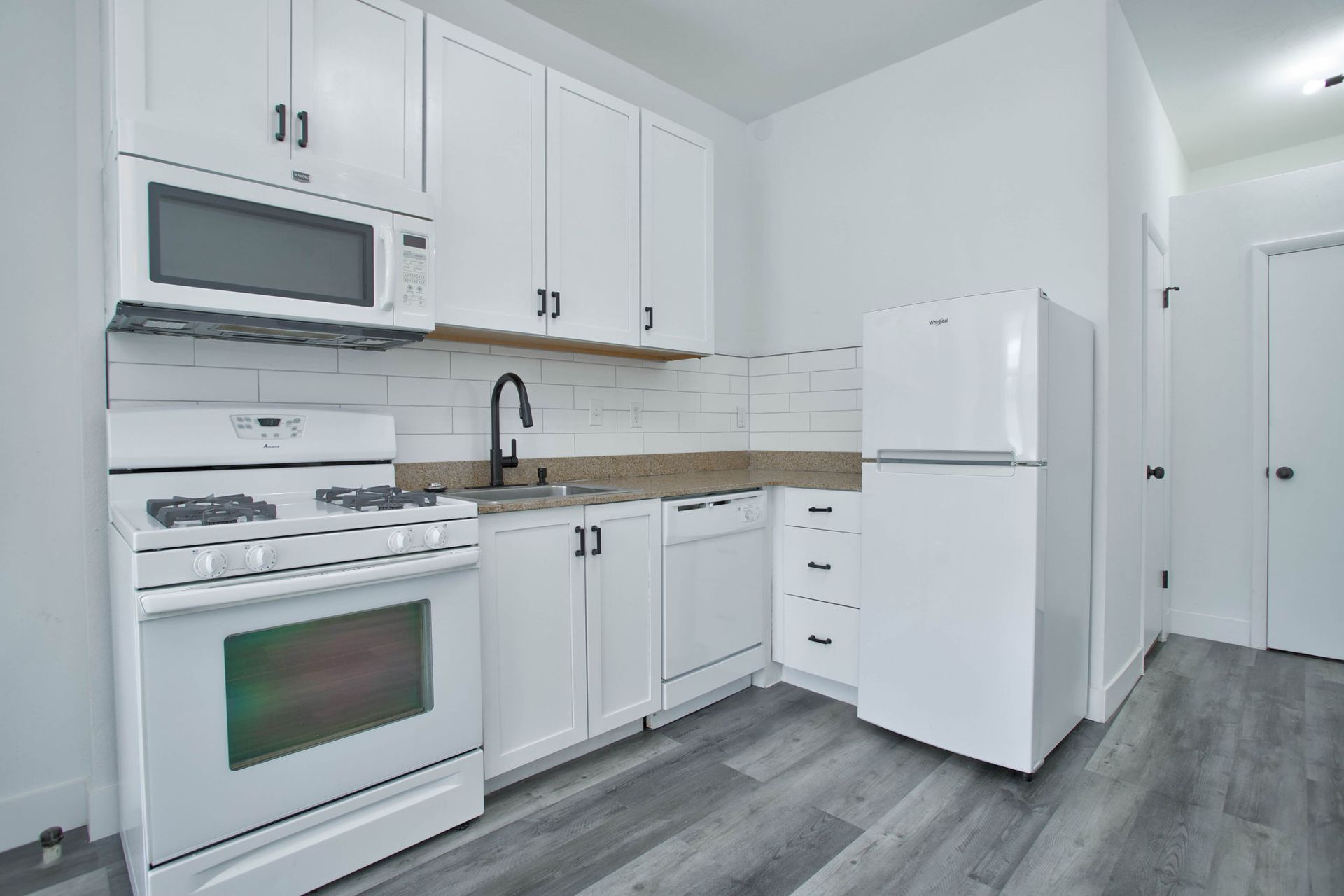 a kitchen with white cabinets , a stove , a refrigerator , and a microwave .