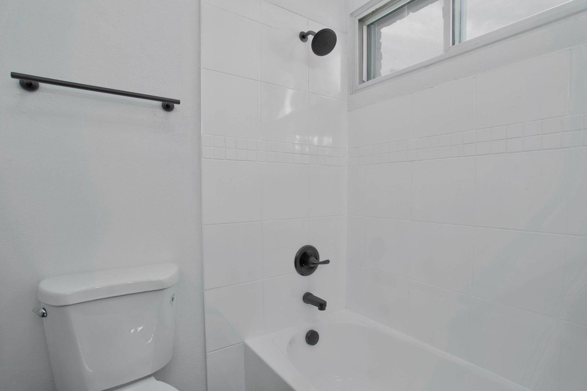 a bathroom with a toilet , bathtub , shower and window .