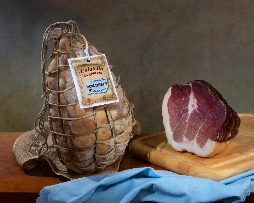 Un pezzo di prosciutto è appoggiato su un tagliere accanto a un sacchetto di prosciutto