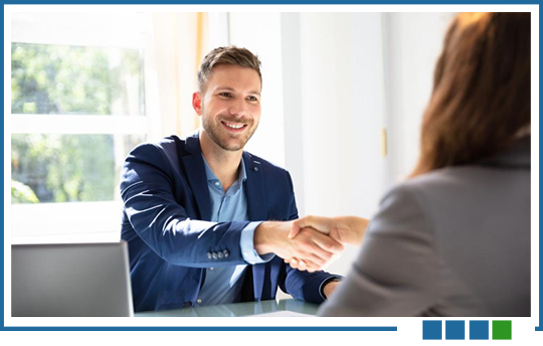 Man in blue blazer shakes hands with a person in a gray suit; smiles in bright office.
