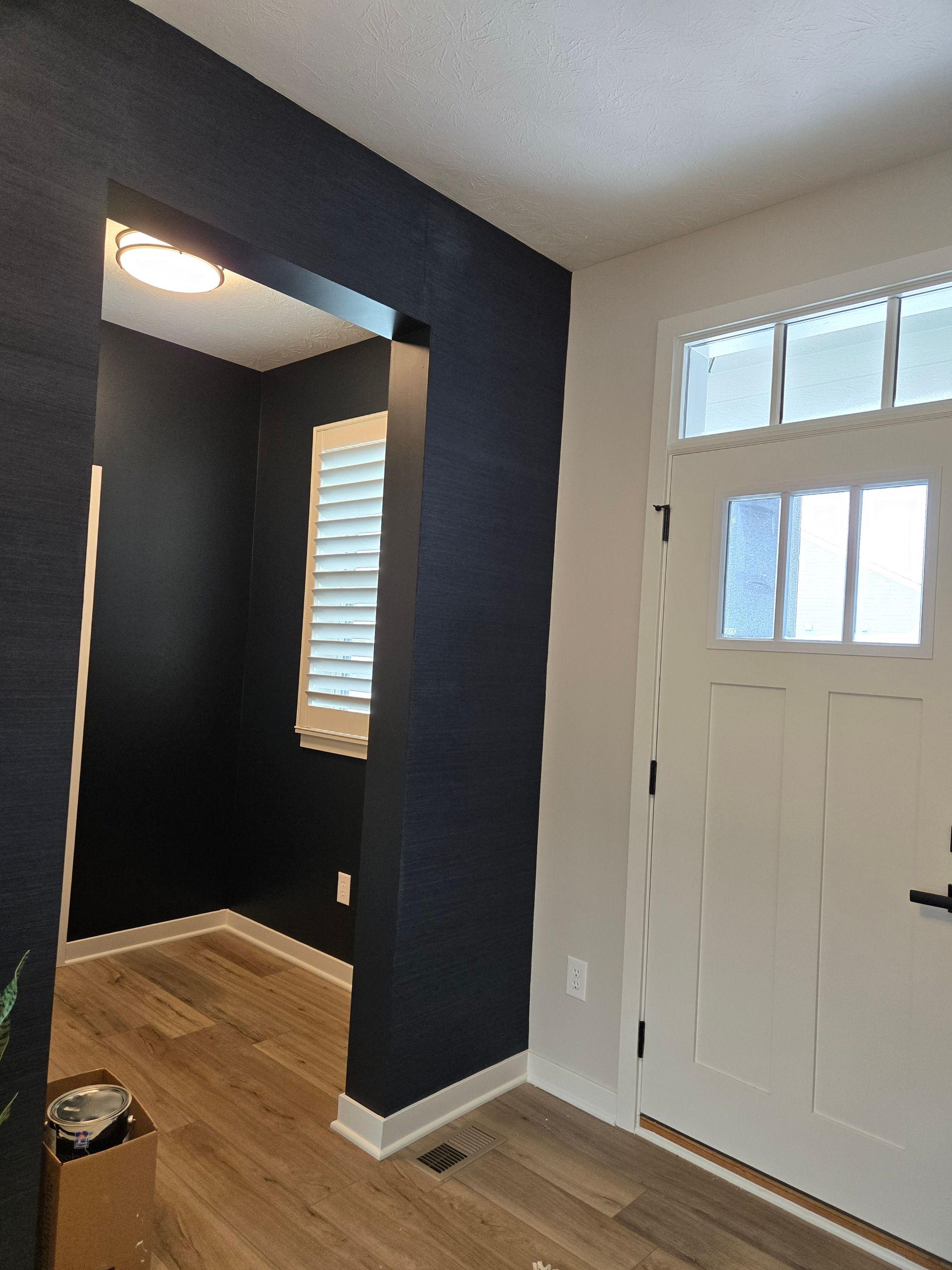 Entryway with a dark blue accent wall, white door, and light brown wood flooring.