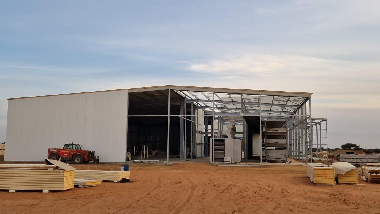 Un grand bâtiment est en construction au milieu d'un champ de terre.