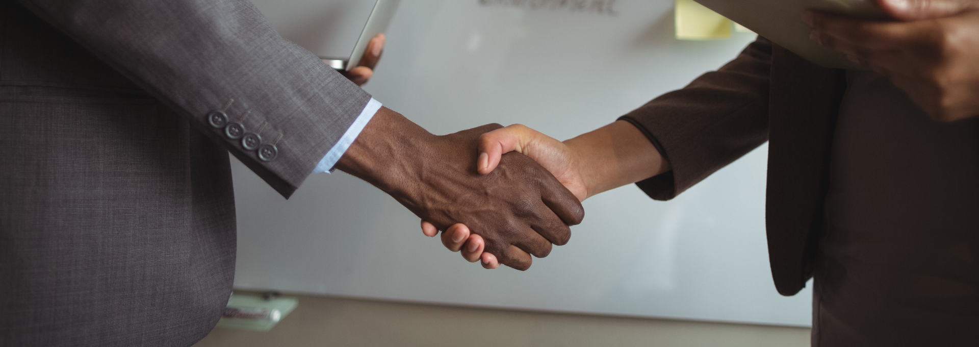 Deux personnes se serrant la main, toutes deux vêtues de vestes de costume, avec un mur blanc en arrière-plan.