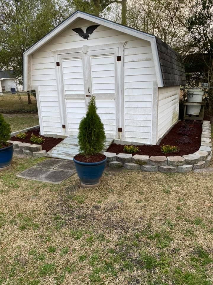 A white barn shed is sitting in the middle of a grassy yard.