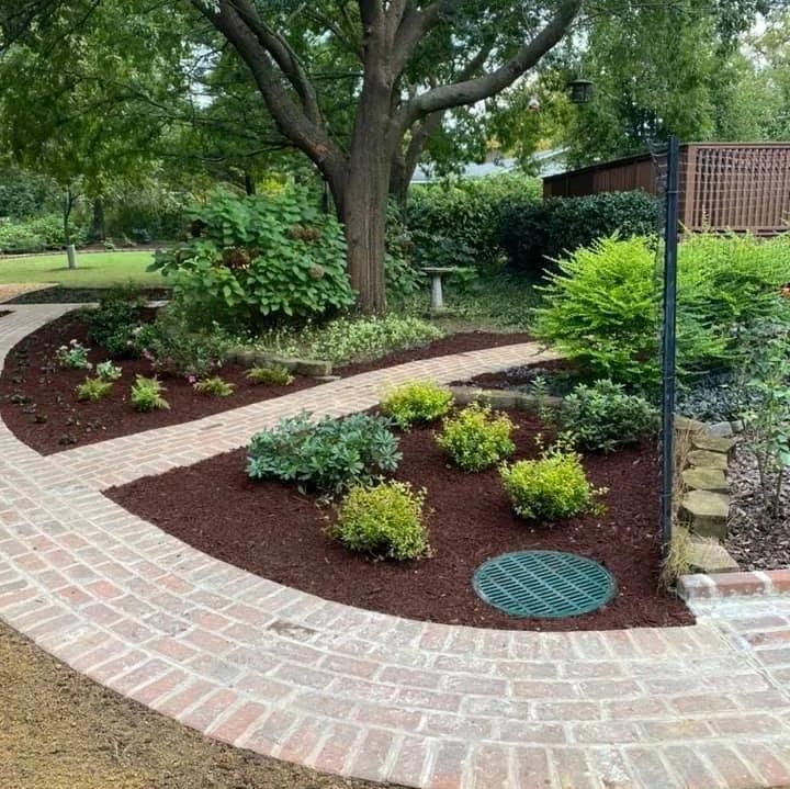 A brick walkway in a garden with a green manhole cover