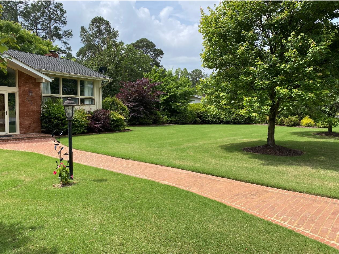 A house with a large lawn and a brick walkway leading to it.