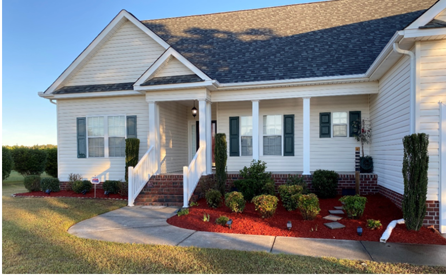A white house with a porch and red mulch in front of it