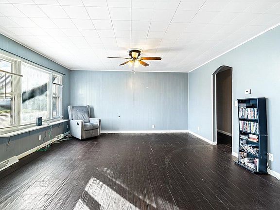 A living room with a ceiling fan , a chair , and a bookshelf.