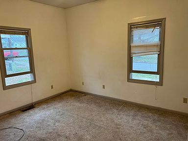 An empty room with two windows and a carpeted floor.