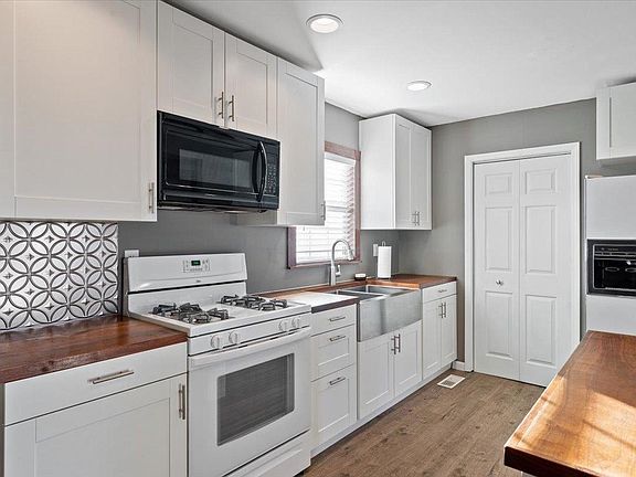 A kitchen with white cabinets , a stove , a sink , and a microwave.