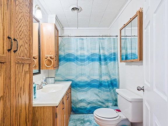A bathroom with a toilet , sink , mirror and shower curtain.