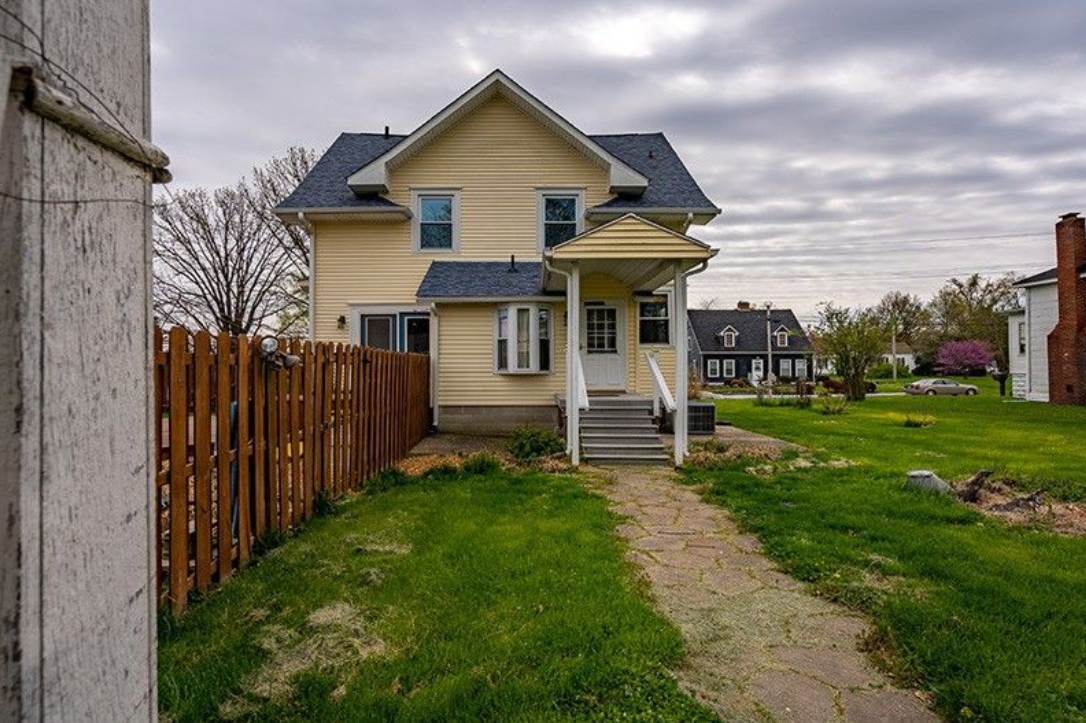 A yellow house with a wooden fence and a path leading to it.