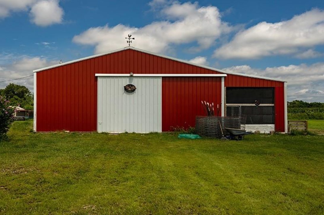 A red barn with a white door is sitting in the middle of a grassy field.