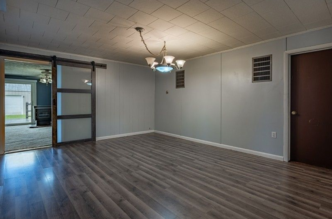 An empty living room with a sliding barn door and a chandelier.