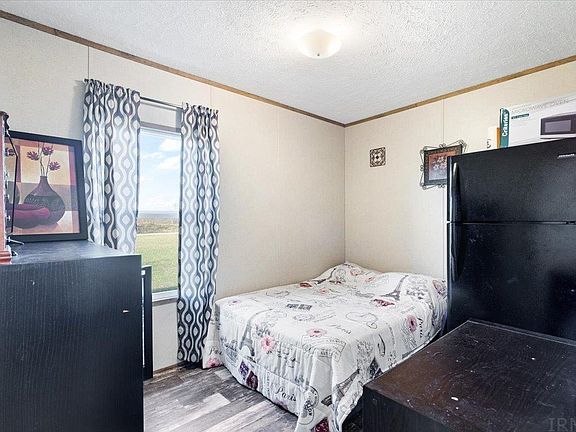 A bedroom with a bed , refrigerator , microwave and window.