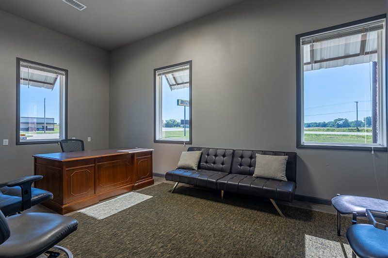 A room with a desk , couch , chairs and windows.