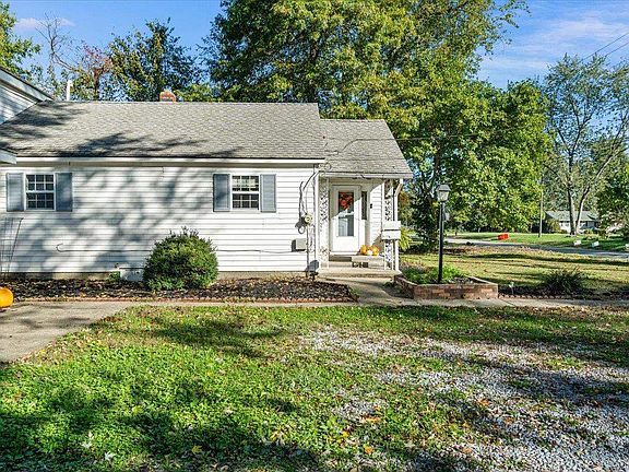 A white house with a gray roof is sitting on top of a lush green field.