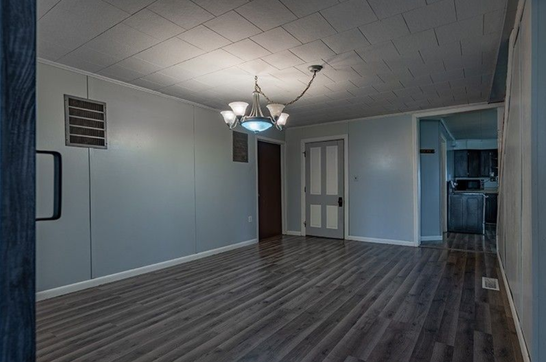 An empty living room with a chandelier hanging from the ceiling.