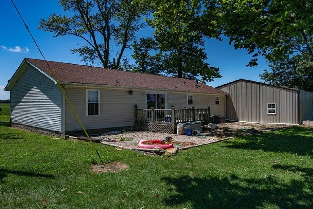 A white house with a brown roof is sitting on top of a lush green field.